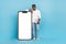 Full body photo of smiling skilled freelancer lean on big smartphone display isolated on blue color background