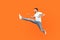 Full body portrait of excited brunette man jumping over in air, running quickly fast. isolated on orange background