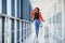 Full body profile portrait of happy female traveler walking with suitcase bag and cellphone