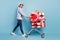 Full body profile side photo of happy brown haired man wear jeans presents box trolley ride isolated on blue color