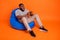 Full body profile side photo of young african guy sit chair addicted station weekend  over orange color