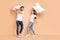 Full body profile side photo of young couple play pillow battle fight happy positive smile excited isolated over beige