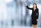 Full body smiling brunette business woman in confident suit, showing at copy space. Blurred office interior background.