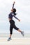 Full body sporty african american woman jumping with hand raised at the beach