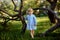 Full body view portrait tiny girl in blue jeans dress, smiling and looking to camera, walking among curved weird trees. Summer