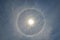 Full circle rainbow around Sun at noon, rays catch the thin vapour formed of ice crystals