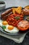 Full English breakfast with bacon, sausage, fried egg, baked beans, hash browns and mushrooms in black plate. cup coffee.