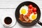 Full english breakfast in frying pan with fried eggs, bacon, beans, tomatoes and coffee on white wooden background