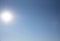 Full frame blue sky, bright disk of the sun and a small silhouette of a paraglider