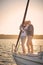 Full leghth of beautiful happy senior couple in love standing on the side of sail boat floating in sea at sunset, they