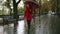 Full legth of female person in red walk under rain with umbrella. Red haired woman wearing red coat with umbrella