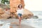 Full-lengh photo of pretty blonde girl with long hair walking on the beach near sea. She wears white shirt with naked