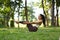 Full length of active millennial woman doing half boat or Ardha Navasana yoga pose on green grass. Healthy lifestyle