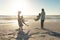 Full length of african american parents spinning children at beach against sky on sunny day