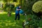 Full length of biracial senior man wearing rubber boots and gloves watering plants with can in yard