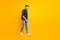 Full length body size photo of cheerful attractive guy walking towards sales wearing sneakers isolated over yellow vivid