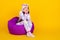 Full length body size photo childish girl wearing pajama sitting in beanbag isolated bright yellow color background