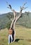 Full length of a charming south asian young guy looking sideways posing with arms crossed while leaning against tree in hilly area