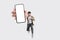 Full length of cheerfull Asian man jumping and smiling in air with showing cellphone blank screen with empty space for mobile app