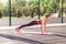 Full length, fit beautiful woman in tight pants practicing yoga on mat outdoor summer day, doing perfect plank asana