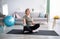 Full length of fit mature woman in sportswear doing strength exercises with dumbbells on yoga mat at home, blank space