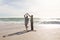 Full length of happy retired senior multiracial couple dancing on shore at beach during sunny day