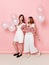 Full length image of happy two girl, dressed in a white, holdings a balloons, over pink background.