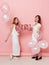 Full length image of a two of happy young women, dressed in a white, holdings a balloons, over pink background.