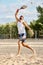 Full-length image of young bearded man in sunglasses playing beach tennis, hitting ball with racket. Summertime outdoor