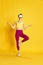 Full-length image of young slim woman wearing vr glases and training against yellow studio background. Yoga and