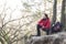 Full length of male hiker crouching on cliff in forest