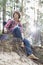 Full length of male hiker looking away while sitting on cliff in forest