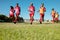 Full length of multiracial male athletes in red uniforms running on grassy land against clear sky