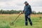 Full length outdoor portrait of numismatist in jacket and cap, holding in hands shovel and metal detector, looking for gold or