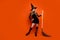 Full length photo of adorable pretty lady wear black wizard costume cap holding broomstick empty space isolated orange