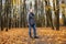 Full length photo of aged man walking along path in golden forest. Fallen dry yellow maple leaves everywhere.