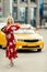 Full-length photo of blonde woman in red dress stopping taxi on summer.