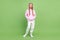 Full length photo of cheerful cool positive young small girl enjoy hold hands pockets hoodie green color background