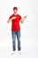 Full length photo of cheerful courier in red t-shirt and cap presenting copyspace text or product with pointing fingers aside and