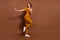 Full length photo of cheerful positive cool young woman dance wear look empty space isolated on brown color background