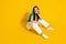 Full length photo of cheerful thoughtful girl dressed white trousers sitting floor looking empty space isolated yellow