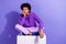 Full length photo of cool indifferent guy dressed violet hoodie siting on white platform arm on chin isolated on purple
