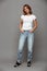 Full length photo of cute brunette woman with hands in her pockets wearing trendy mom jeans and white tshirt, looking at camera