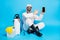 Full length photo of doctor man sit floor point finger smartphone virtual technology have spray sprayer sanitize wear