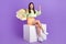 Full length photo of ecstatic overjoyed girl wear stylish pullover sit on platform buy new clothes isolated on violet
