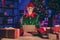 Full length photo of elf sit floor type greeting on laptop wear green glasses cap in house indoors with evening x-mas