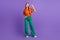 Full length photo friendly and peaceful ginger lady in orange t shirt green pants makes v sign to you isolated on purple