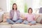 Full length photo of happy calm peaceful siblings sisters sit sofa meditation indoors inside house home