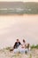 The full-length photo of the newlyweds having the wedding picnic at the background of the river during the sunset.