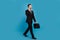 Full length photo of professional personal agent seller manager young man call phone walking briefcase isolated on blue